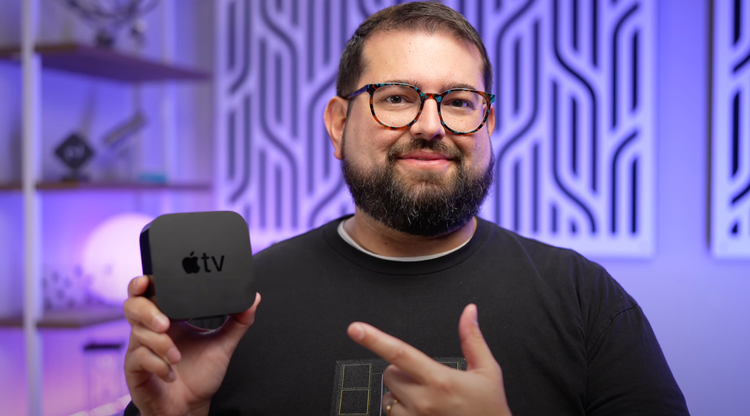 Stephen Robles holding an Apple TV hardware box and pointing at it.