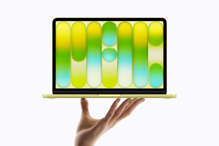 A promotional photo of a hand holding up a Citrus coloured Apple MacBook Neo