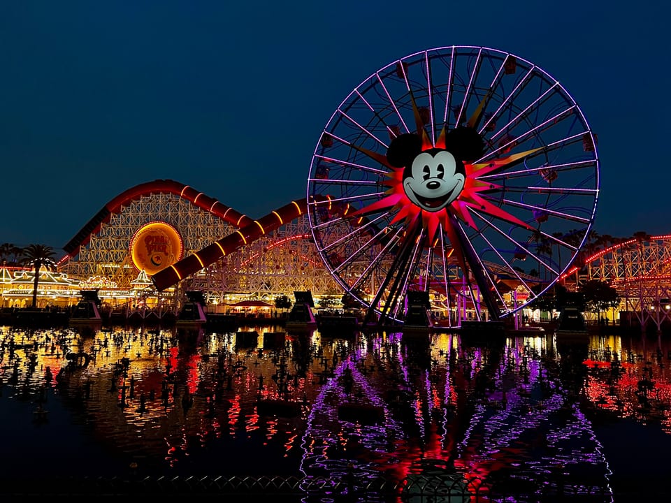 A photo of Disneyland's Ferris Wheel with Mickey Mouse's head at the centre and a rollercoaster in the background at night.